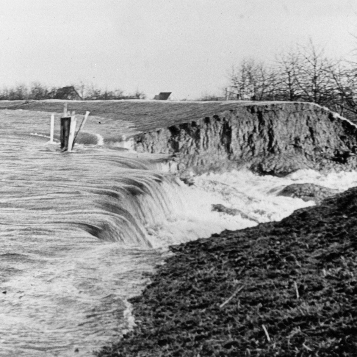 Historische Aufnahme eines Deichbruchs mit einsrömendem Wasser.